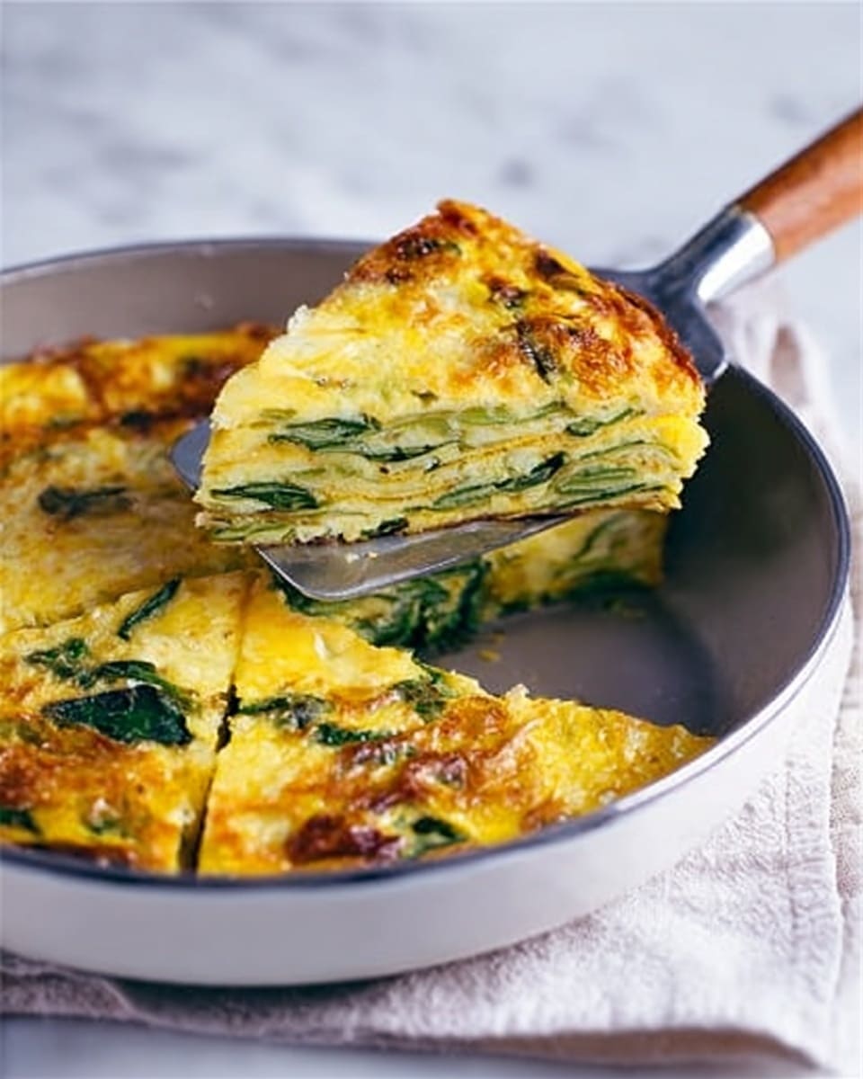 The image shows a thick slice of a golden-yellow frittata being lifted from a white frying pan with a silver spatula that has a wooden handle. The frittata has at least three visible layers: a top layer of melted and slightly browned cheese with green spinach leaves scattered throughout, a middle layer of pale yellow eggs mixed with green vegetables, and a bottom layer that appears firm and cooked through. The interior layers reveal the texture of cooked eggs and pieces of spinach. The pan sits on a soft white cloth over a white marbled surface. The photo taken with an iphone --ar 4:5 --v 7