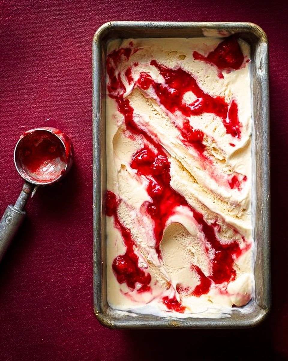The image shows a rectangular metal baking pan filled with creamy white ice cream swirled with bright red strawberry sauce in uneven patches and streaks across the top. The ice cream looks smooth and soft, with the red sauce adding bright, glossy spots and lines that contrast with the pale cream. Next to the pan on the left, an old metal ice cream scoop has some red sauce and cream left on it, resting on a white marbled surface that spreads under the entire setup. The background is a rich dark red, adding warm color. photo taken with an iphone --ar 4:5 --v 7