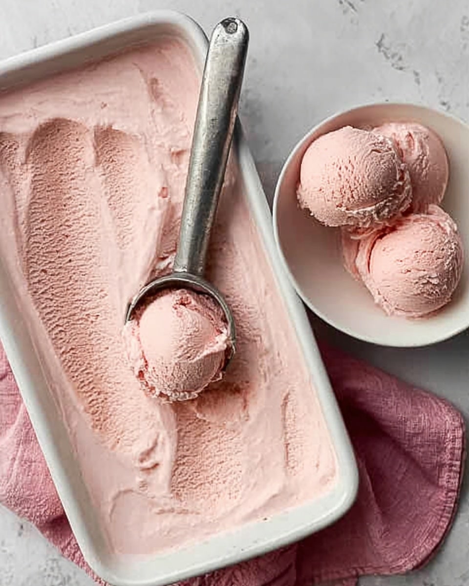 A white rectangular baking dish filled with smooth, pale pink ice cream, with a metal ice cream scoop resting inside it. Next to the dish, a white bowl holds three scoops of the same pink ice cream, showing a creamy and slightly textured surface. Both containers are placed on a white marbled surface with a soft pink cloth under the baking dish. The lighting highlights the creamy texture of the ice cream. Photo taken with an iphone --ar 4:5 --v 7
