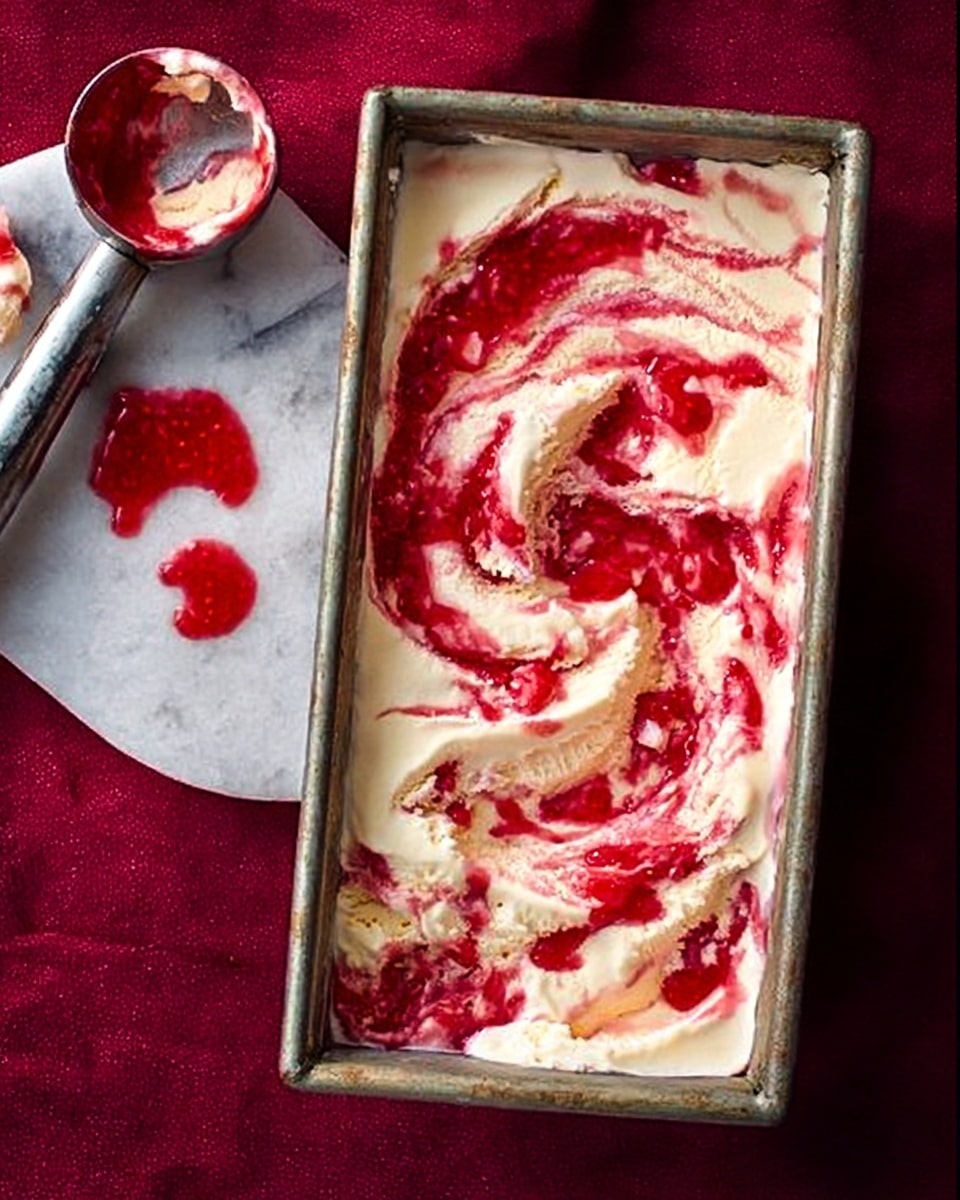 A rectangular metal pan filled with creamy white ice cream swirled with bright red strawberry sauce, creating uneven patches and streaks of red on top. The ice cream surface looks soft and slightly melted in places, showing smooth texture with some creamy lumps. To the left of the pan, there is a metal ice cream scoop resting on a white marbled surface, with some red strawberry sauce left inside it and a small dollop spilled nearby. The background is a rich, dark red fabric with a slightly rough texture. Photo taken with an iphone --ar 4:5 --v 7