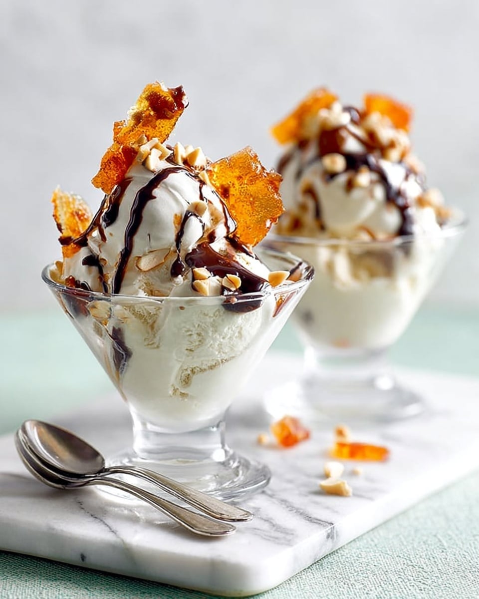 The image shows two clear glass dessert cups filled with creamy white ice cream. Each cup has a generous swirl of smooth white cream on top. On the cream, there are pieces of crispy, brown caramelized sugar shards with an orange tint, adding texture and color. The ice cream and toppings are drizzled with dark chocolate sauce, creating thin lines over the cream and shards. A few pale nuts are scattered on top, adding extra detail. The cups sit on a white marbled surface with two silver spoons in front of them. The background is soft and light, highlighting the dessert. Photo taken with an iphone --ar 4:5 --v 7