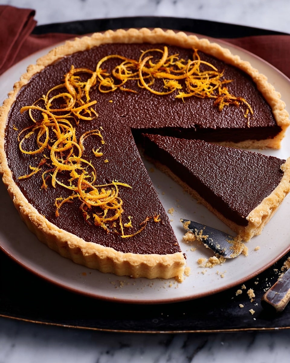 A round tart with one slice cut out and placed next to it shows a thick, dark brown chocolate filling with a smooth but slightly bumpy texture. The crust is light golden brown, crisp and crimped around the edges, forming one layer at the base and sides. Thin, curly orange zest strands are spread decoratively on top of the chocolate layer, providing contrast in color and texture. The tart sits on a white plate with a black tray underneath. A knife with black handle and some crumbs rests beside the tart on a white marbled textured surface. Photo taken with an iphone --ar 4:5 --v 7