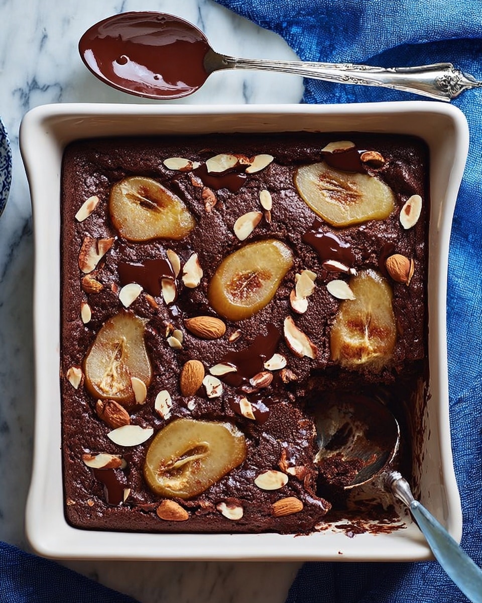 A rectangular white baking dish holds a rich chocolate cake baked with slices of light yellow pear embedded within the top layer, scattered irregularly. The dark brown cake surface is textured, slightly cracked, and sprinkled with toasted sliced almonds, adding a light cream color and a crunchy look. Dark brown melted chocolate chunks are partially melted and visible on the surface among the pears and almonds. A silver spoon with dark chocolate remains on it rests above the dish on a white marbled surface with a blue cloth underneath. Part of the cake is scooped out from one corner, showing the moist inside. Photo taken with an iphone --ar 4:5 --v 7