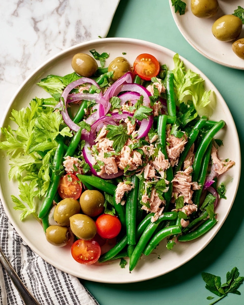 A fresh salad is shown on a white plate, placed on a white marbled surface. The salad has a base layer of long green beans scattered across the plate, mixed with light green celery leaves. On top, there are chopped pieces of light pink tuna, slices of thin red onion rings, and bright green olives spread evenly. Small shiny red cherry tomatoes and fresh parsley leaves add more color, scattered nicely across the salad. The overall look is vibrant with mainly green, red, and light pink tones, giving a fresh and healthy feel. photo taken with an iphone --ar 4:5 --v 7