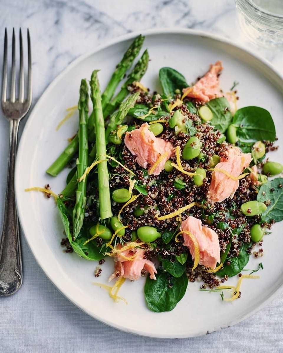 A white plate on a white marbled surface holds a fresh, colorful salad made of three main layers: a base of mixed black and white quinoa with scattered green edamame beans, topped with bright green asparagus spears and fresh spinach leaves, and finished with several pieces of pink salmon flakes garnished with thin yellow lemon zest strips. The textures range from the soft salmon and tender asparagus to the slightly crunchy quinoa and edamame, all arranged to create a vibrant, healthy dish. A woman's hand reaches from the left side, holding a glass above the plate, with a silver fork placed to the right. Photo taken with an iphone --ar 4:5 --v 7