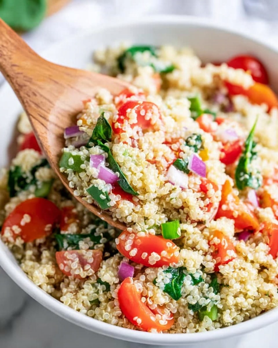 A close-up image of a white bowl filled with a grain salad, featuring light yellow quinoa as the main layer. Mixed evenly throughout are halved bright red cherry tomatoes, small diced green bell peppers, finely chopped purple red onions, and fresh green spinach leaves. A wooden spoon is scooping a large portion from the bowl, showing the fluffy texture of the quinoa combined with the fresh, colorful vegetables. The bowl is placed on a white marbled surface, giving a clean and fresh look. photo taken with an iphone --ar 4:5 --v 7
